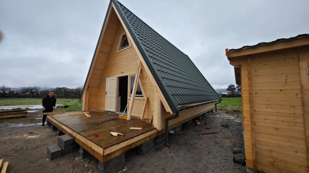 Casa A-Frame em madeira fechada, com cobertura verde, caleiras, porta e janelas montadas