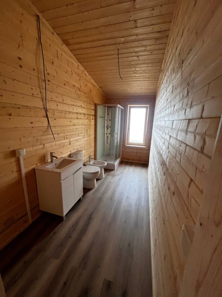 Casa de banho de casa de madeira com móvel de lavatório, sanita, bidé e cabine de duche com hidromassagem