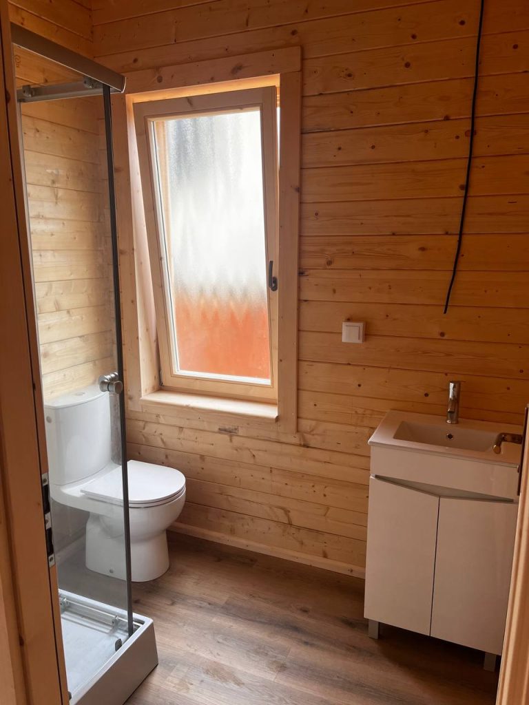 Casa de banho compacta em madeira com base de duche, sanita, lavatório e janela oscilobatente de vidro fosco
