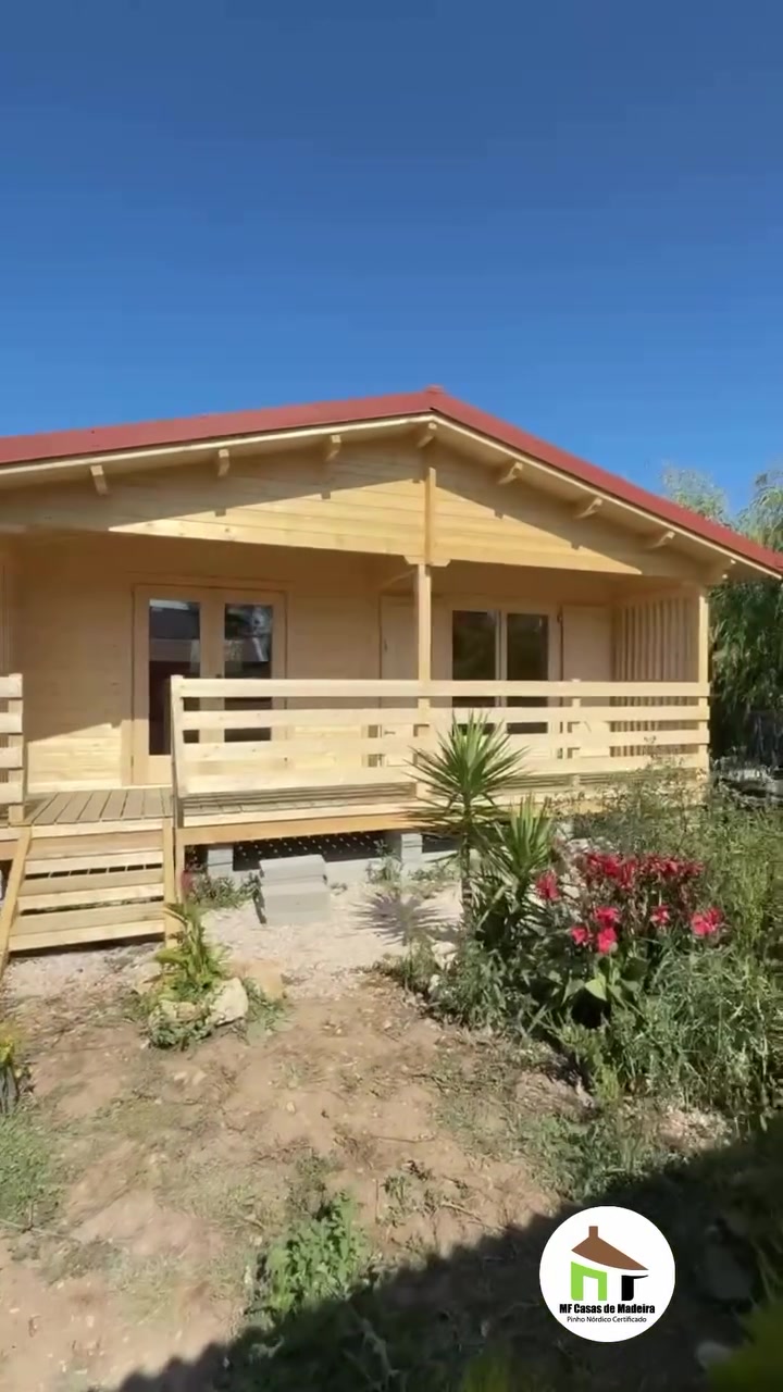 Fachada da casa de madeira com varanda, guardas em madeira e canteiros de flores