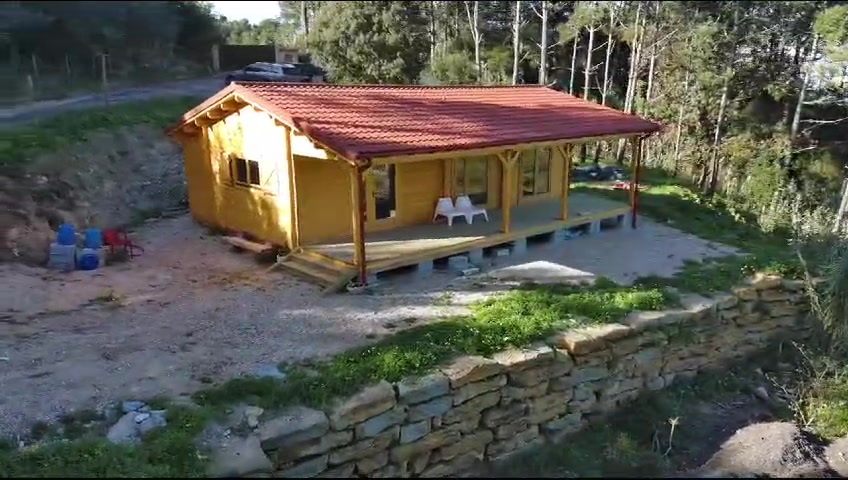 Casa de madeira com alpendre sobre plataforma em gravilha e muro de pedra