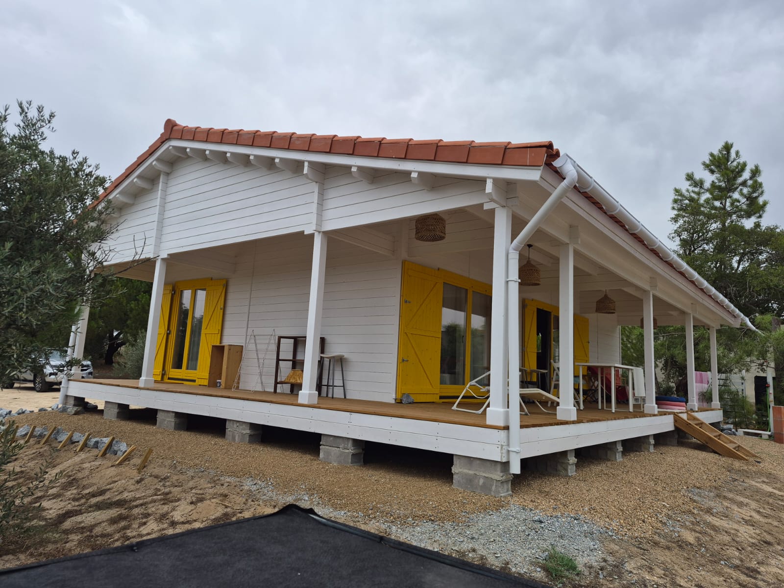 Casa de madeira pintada de branco com portadas amarelas, colunas brancas e alpendre com deck, obra MF