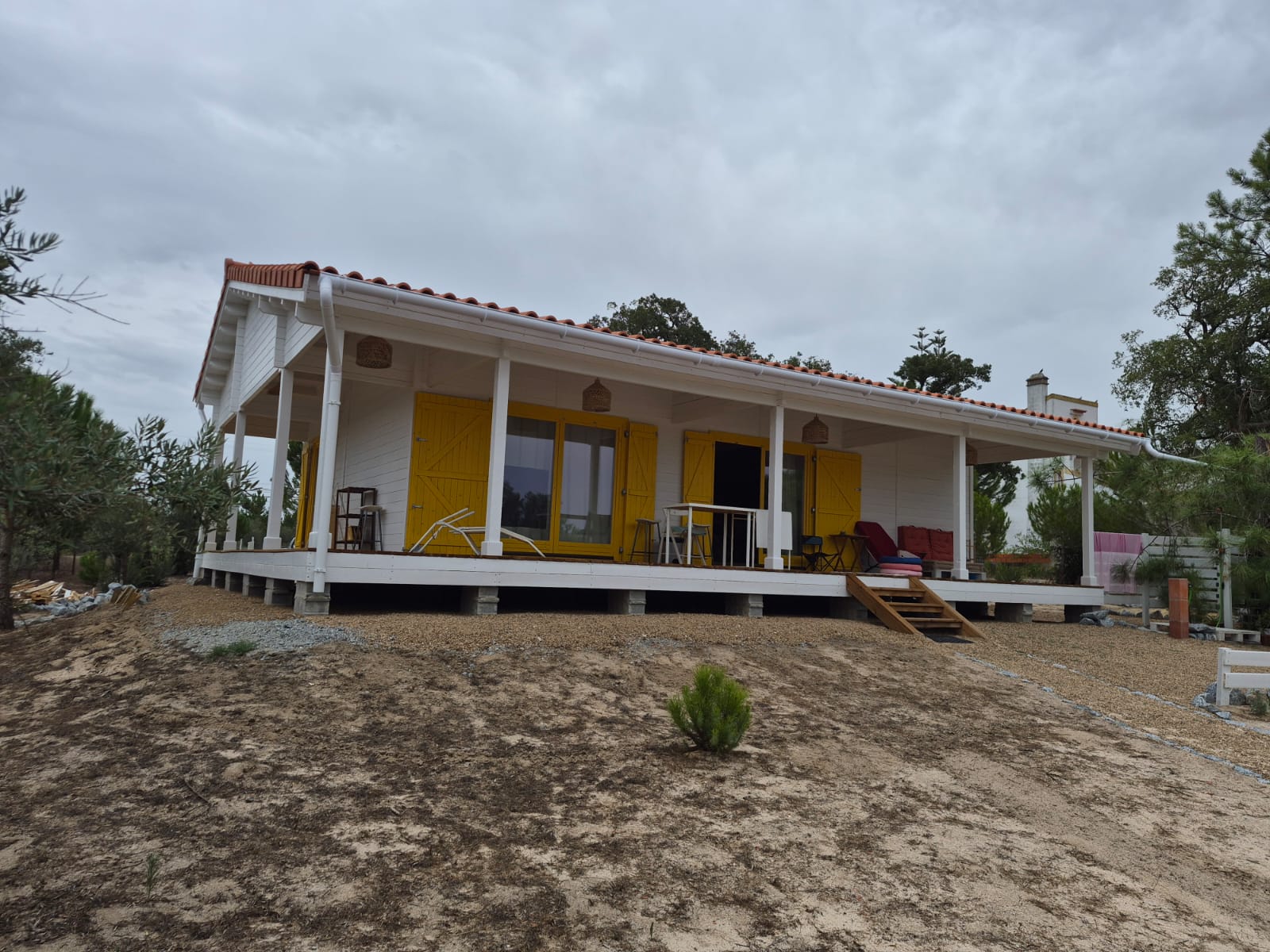 Casa de madeira térrea com alpendre em L, telha cerâmica e casa elevada sobre maciços