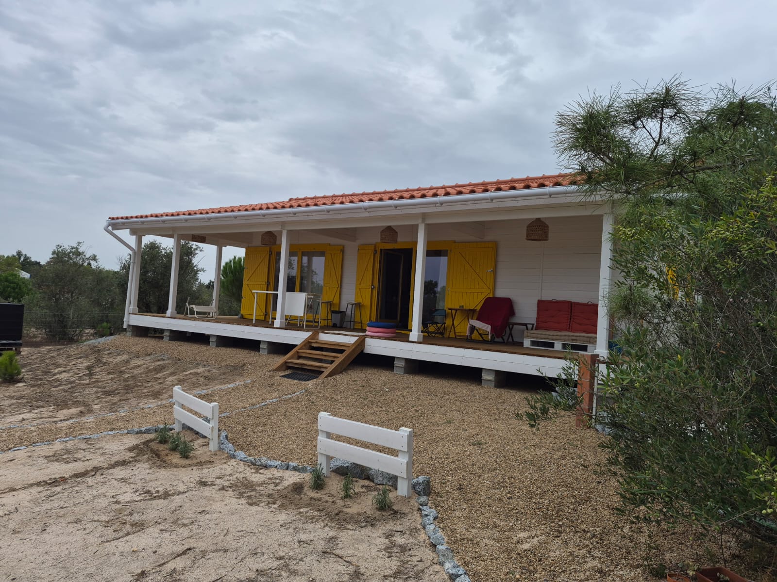 Alpendre coberto da casa de madeira branca, com portas-janela e portadas amarelas