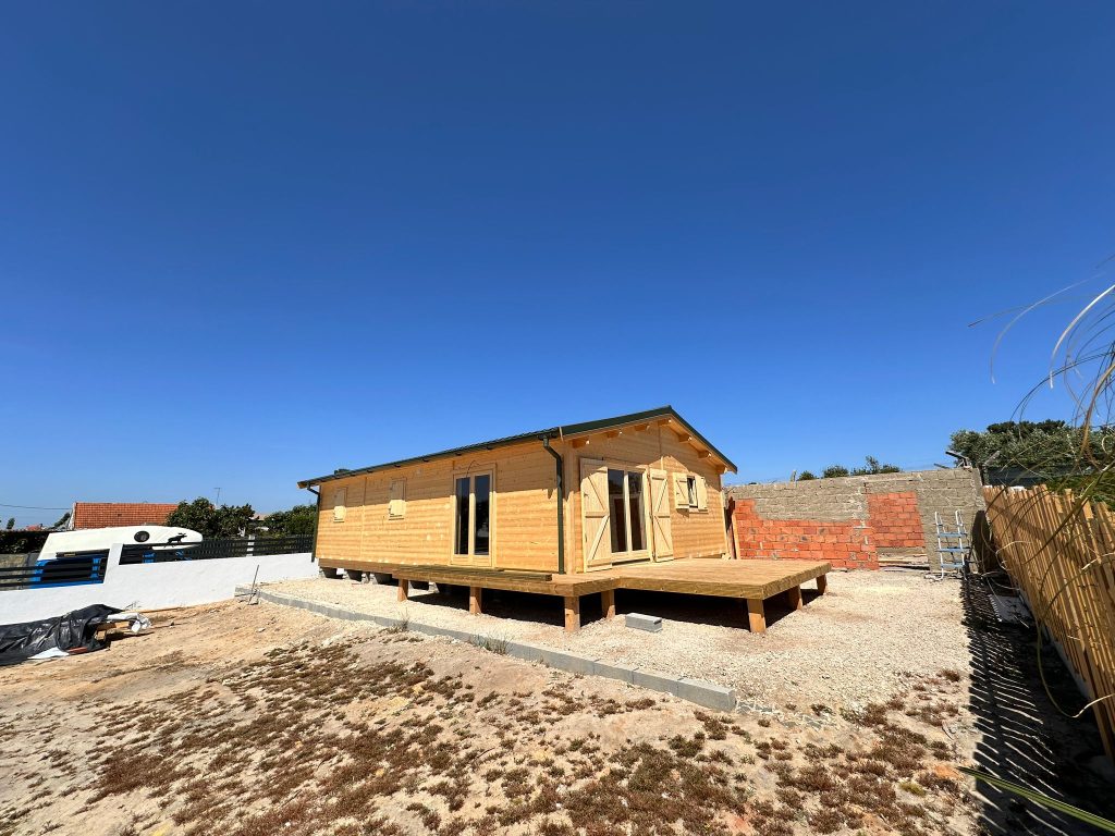 Casa de madeira térrea em pinho natural com deck em madeira, portas envidraçadas e cobertura verde