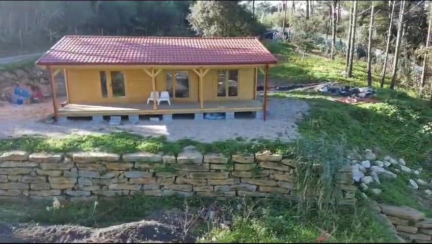 Casa de madeira elevada sobre maciços de betão, com alpendre corrido e guardas