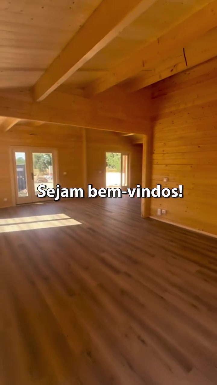 Sala ampla da casa de madeira com vigas à vista e pavimento em tom carvalho