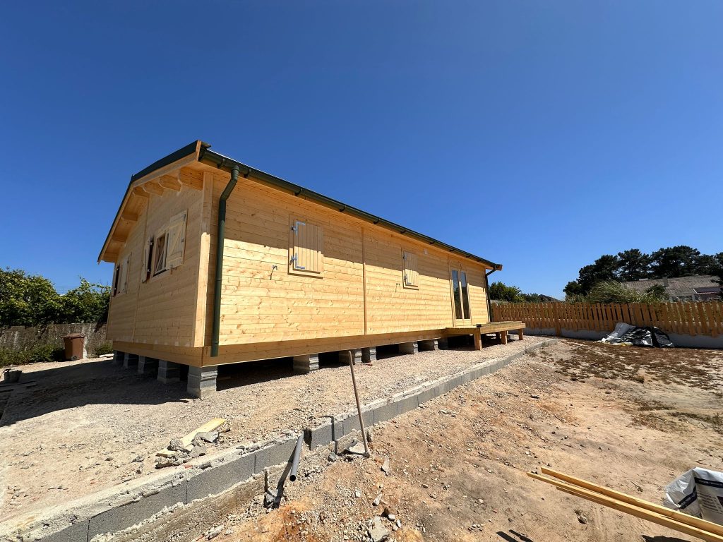 Fachada lateral de casa de madeira maciça elevada sobre pilares com desvão ventilado e caleira verde