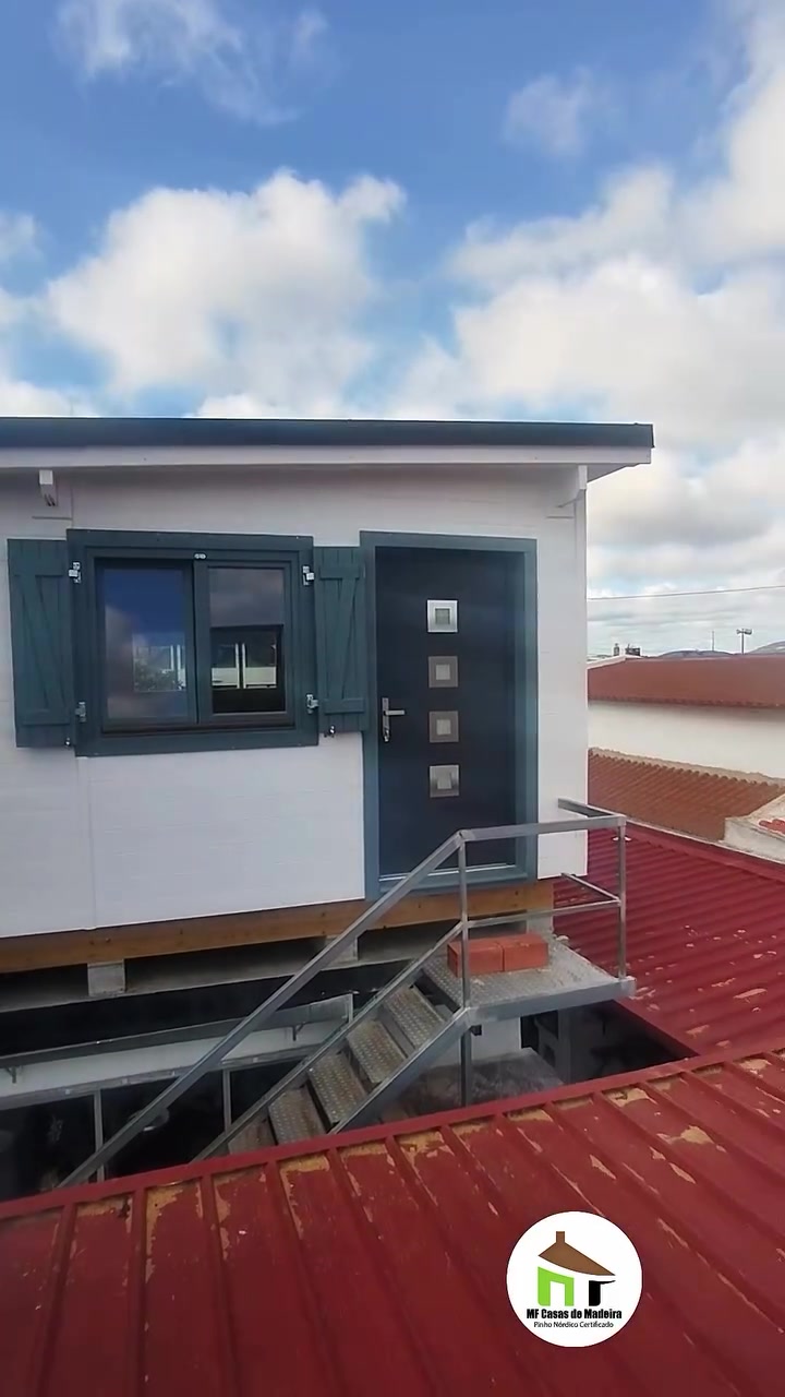 Fachada da casa de madeira T0 pintada de branco, com portadas e porta de entrada antracite