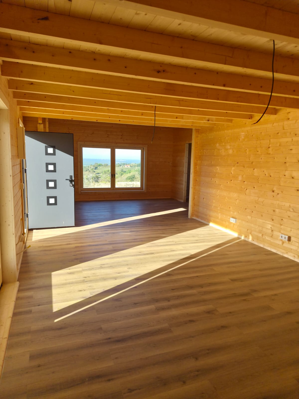 Sala ampla com vigas de madeira à vista e janela com vista para o campo