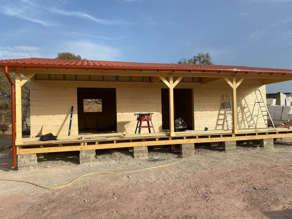 Casa de madeira com cobertura em chapa com aspeto de telha cor de barro, caleiras e alpendre