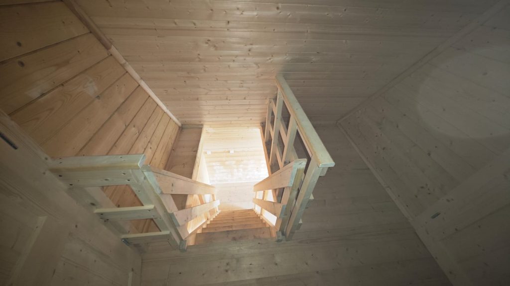 Vista de cima da escada e guarda em madeira do mezanino de uma casa A-Frame