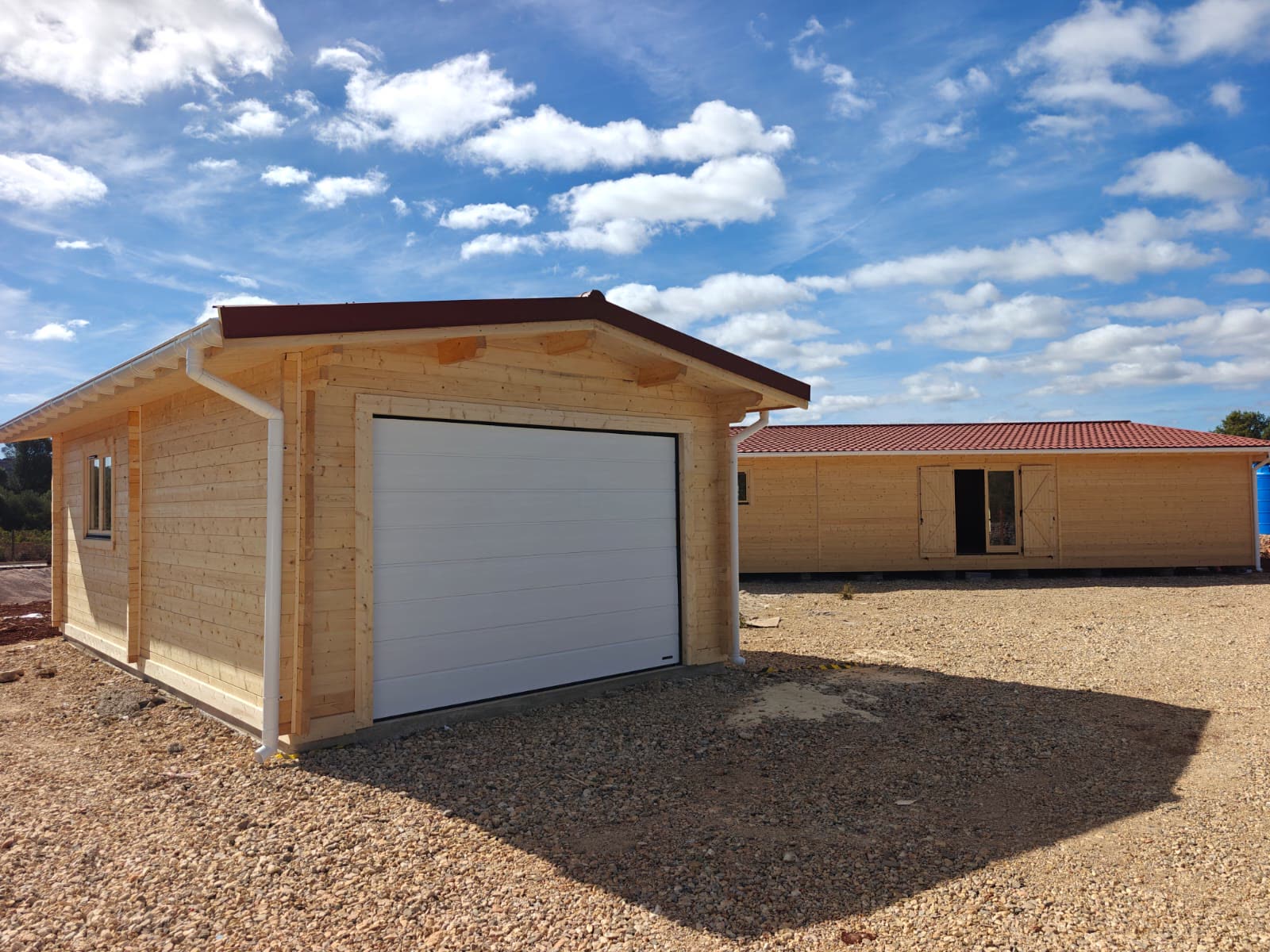 Garagem de madeira com portão seccionado branco e telhado vermelho, construída pela MF Casas de Madeira ao lado da moradia