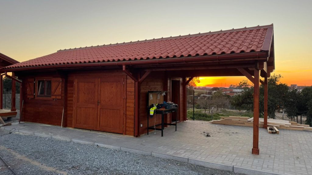 Garagem em madeira maciça com portão de duas folhas e telheiro lateral sobre pavimento em pavê