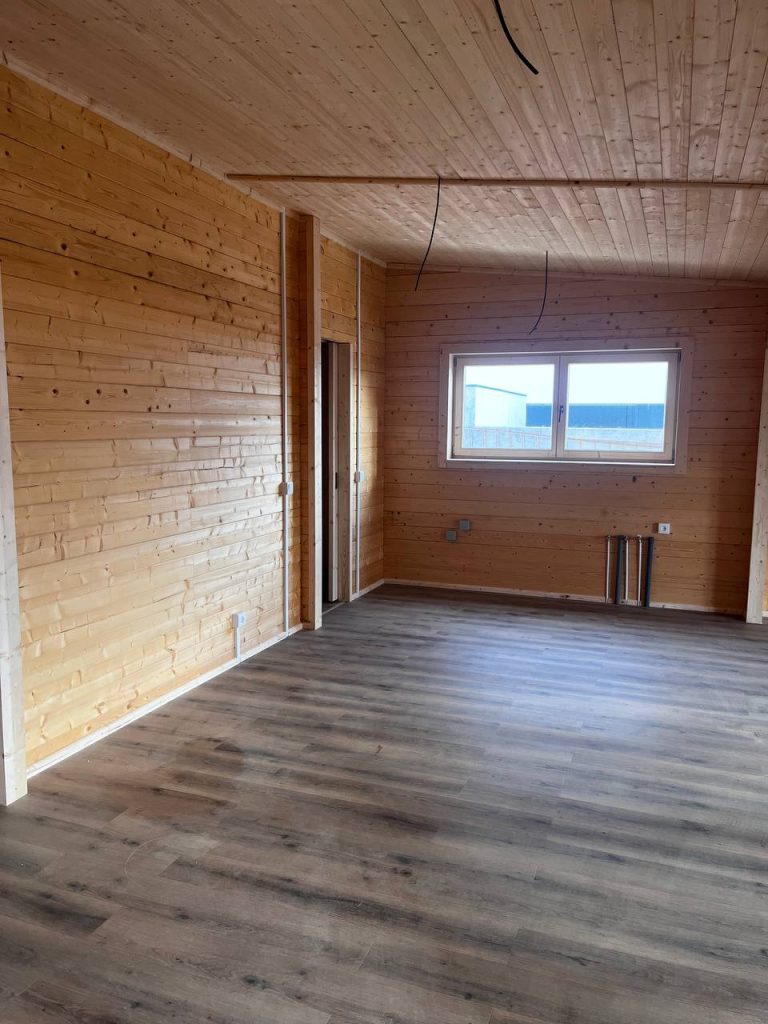 Interior de casa de madeira com paredes em pinho maciço, pavimento vinílico e tubagens para a cozinha