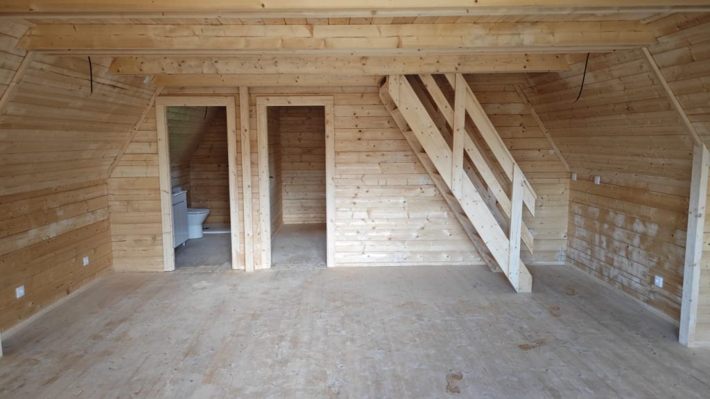 Interior do rés-do-chão de uma casa A-Frame em pinho maciço com escada e portas de madeira