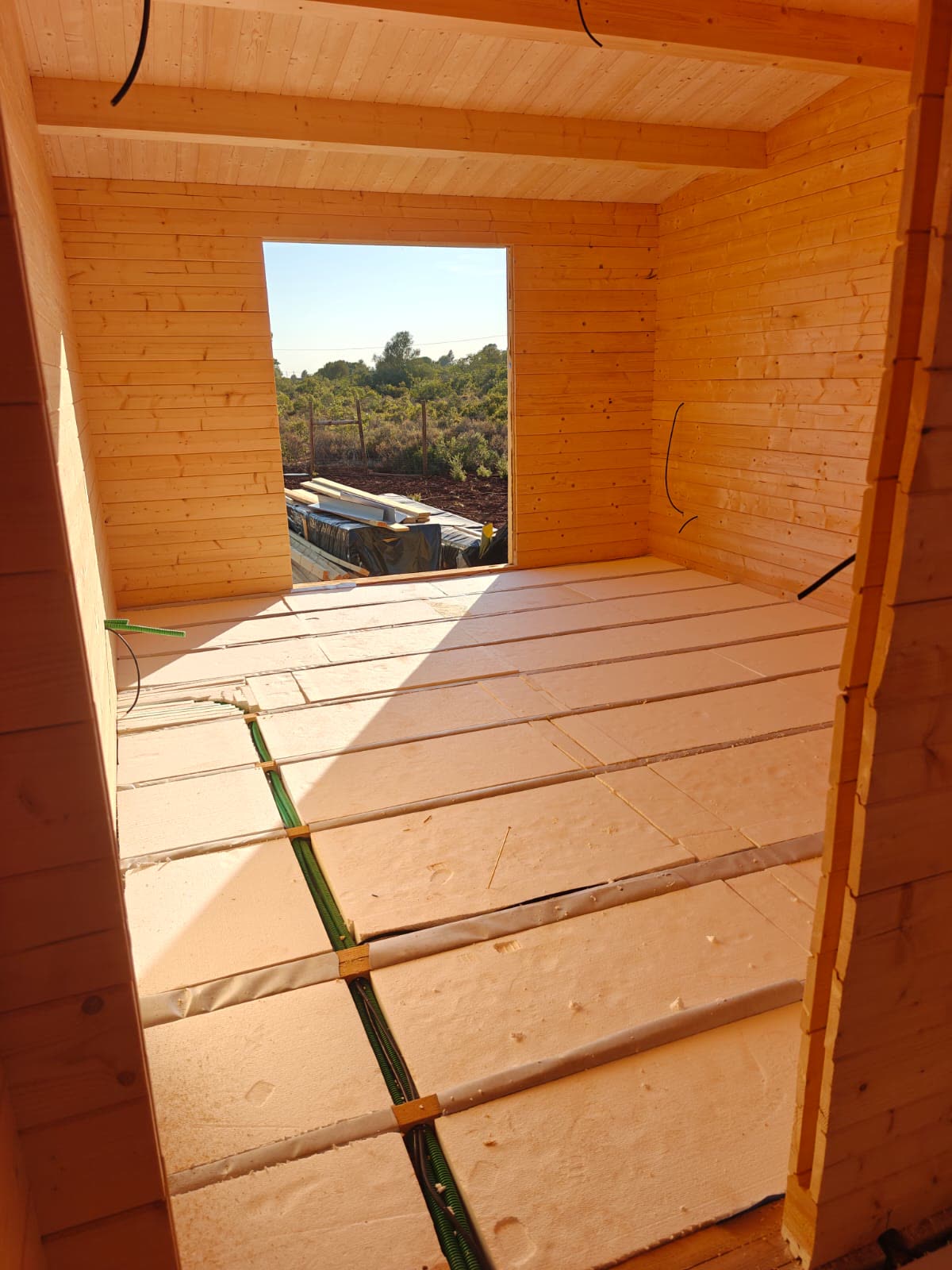 Interior de casa de madeira em obra com placas de isolamento no pavimento e tubagens elétricas embutidas entre as vigas
