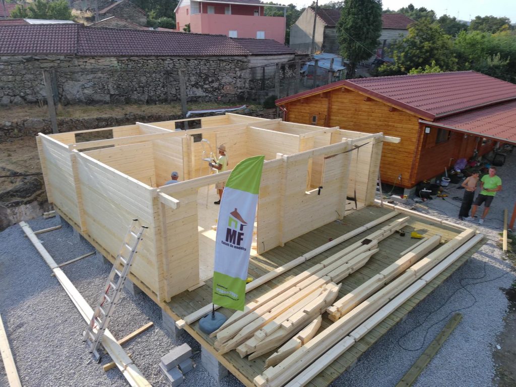Montagem de uma casa de madeira maciça MF: paredes em toros de pinho nórdico e alpendre em deck