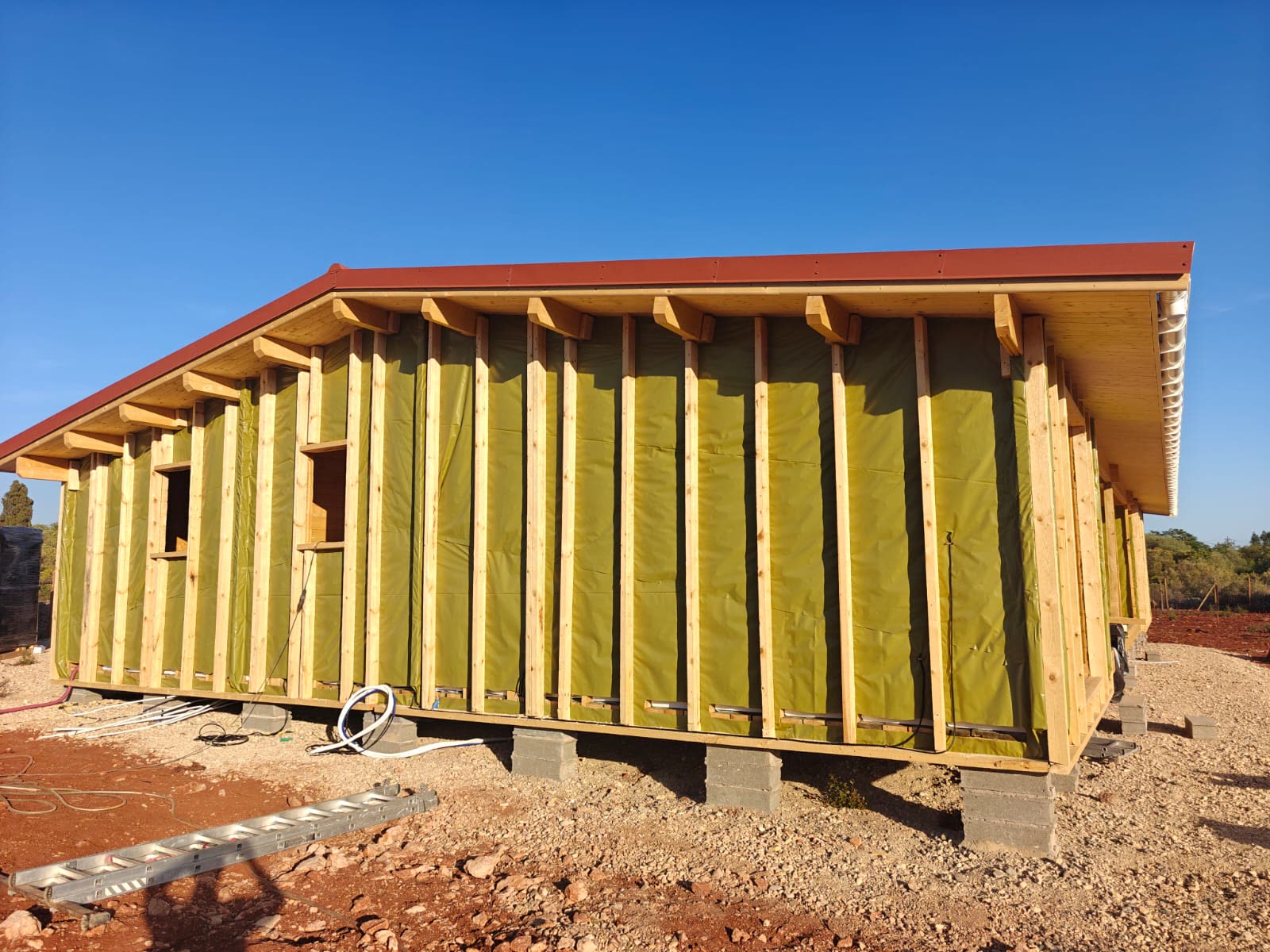 Parede dupla de casa de madeira em construção, com prumos, membrana e beiral da cobertura já com caleira