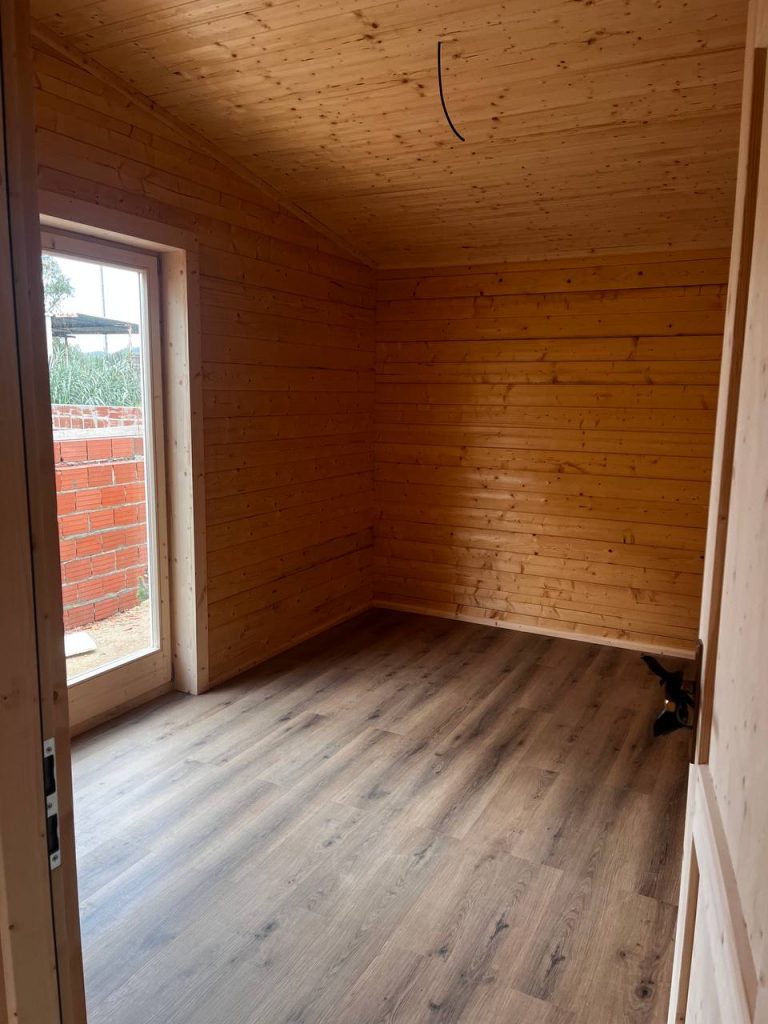 Quarto de casa de madeira maciça com teto inclinado em pinho e porta-janela em madeira