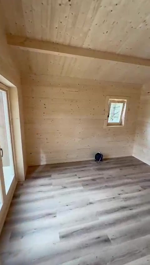Quarto de casa de madeira maciça com teto em pinho, viga à vista e janela em madeira