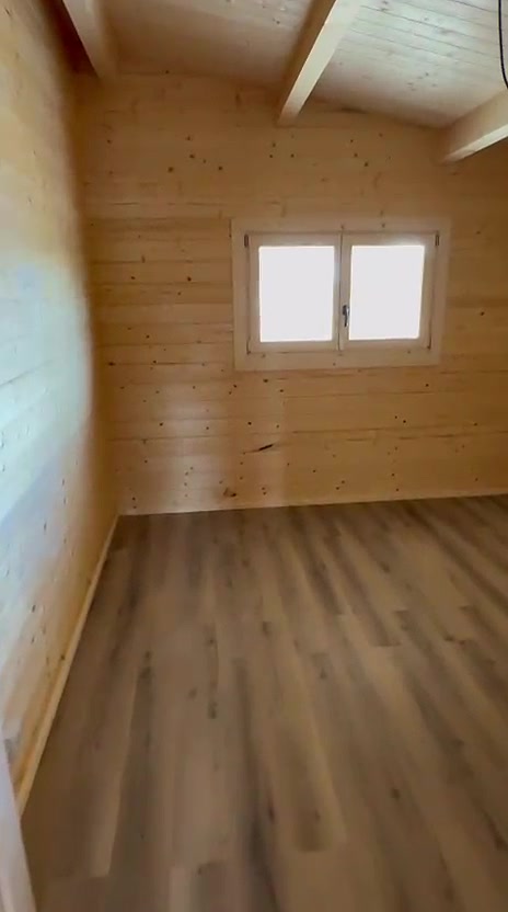 Quarto de casa de madeira maciça com janela em madeira e teto inclinado em pinho