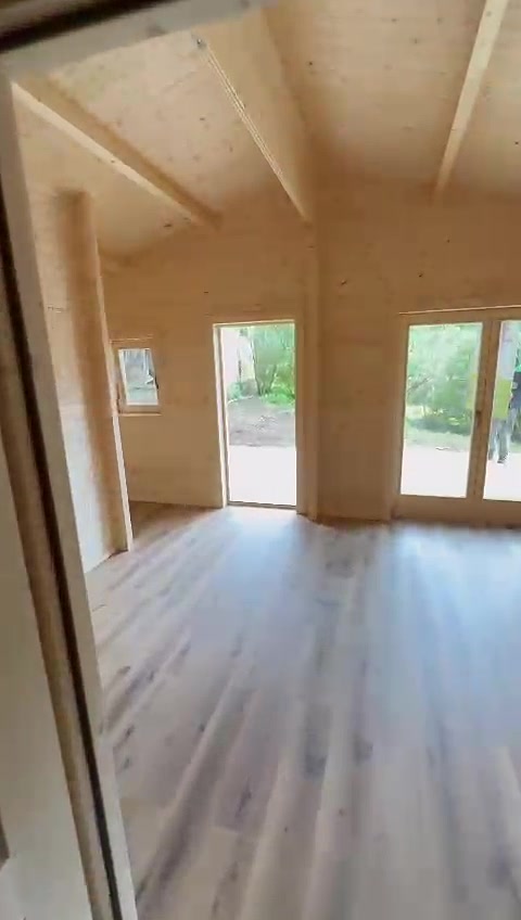 Sala de casa de madeira com teto em pinho, vigas à vista e duas portas envidraçadas para o deck