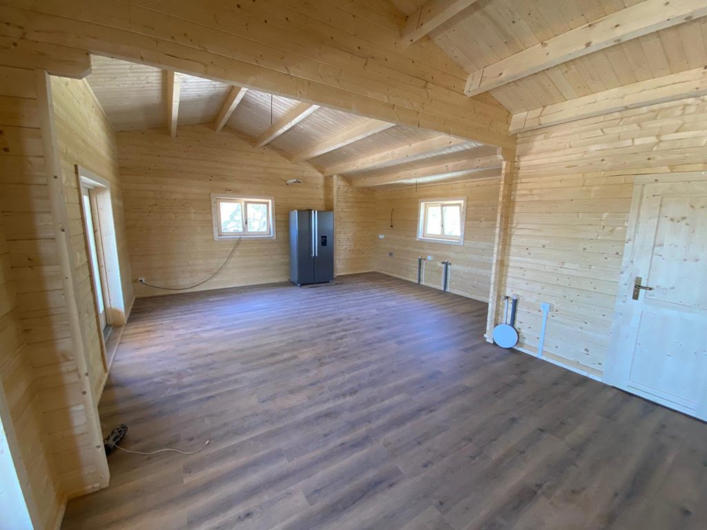 Sala e cozinha em open space de casa de madeira com madres à vista e pavimento vinílico