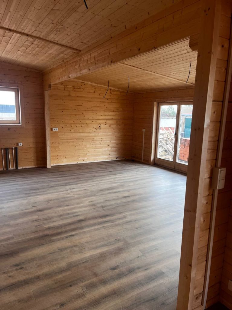 Sala em open space de casa de madeira maciça com teto em pinho, vigas à vista e porta-janela