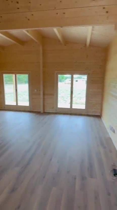 Sala de casa de madeira com teto em pinho, vigas à vista e porta-janela
